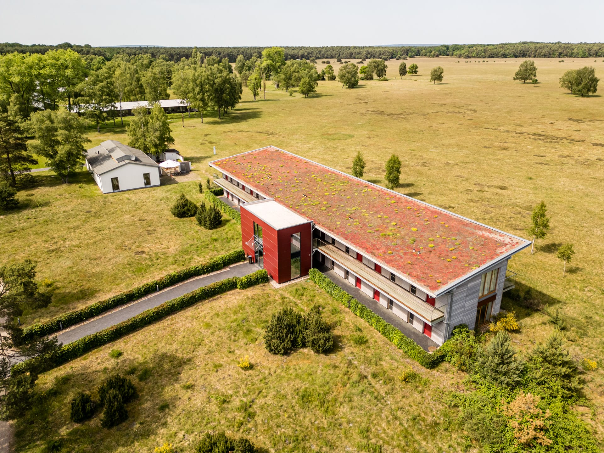 Ein Hotelgebäude des Hotelcamps Reinsehlen, das in einer weiten Graslandschaft mit Bäumen steht. Das Hotelfoto wurde vom Hotelfotografen aus der Luft aufgenommen