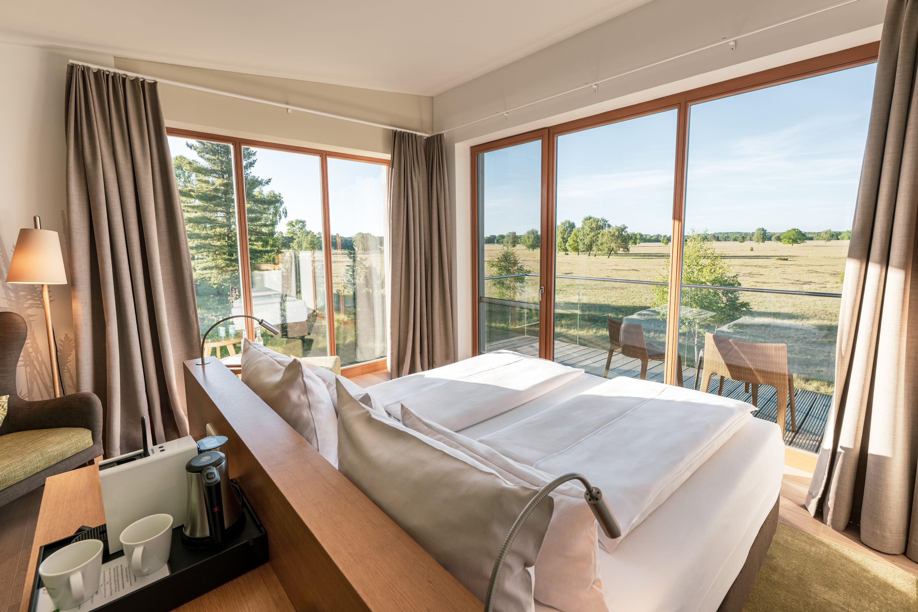 modernes Hotelzimmer mit großen Panorama-Fenstern, die einen freien Blick auf die Terrasse in die Natur und Landschaft bieten.