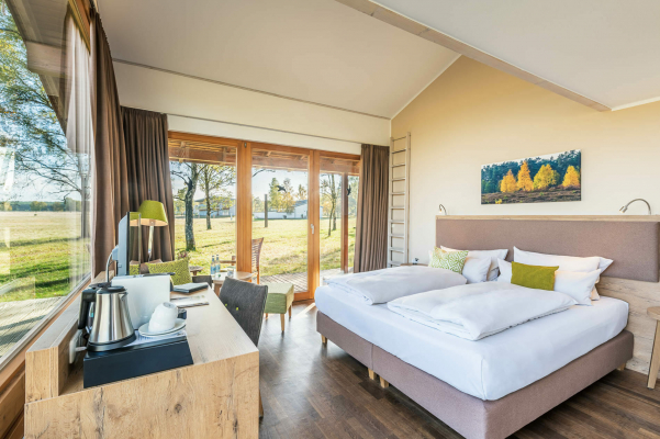Hotel Panoramazimmer - Camp Reinsehlen Naturhotel Camp Reinsehlen in der Lüneburger Heide Panoramazimmer mit Blick auf das Doppelbett und auf die Panoramafenster. Aussagekräftige Fotos für Ihr Hotel-Unternehmen.