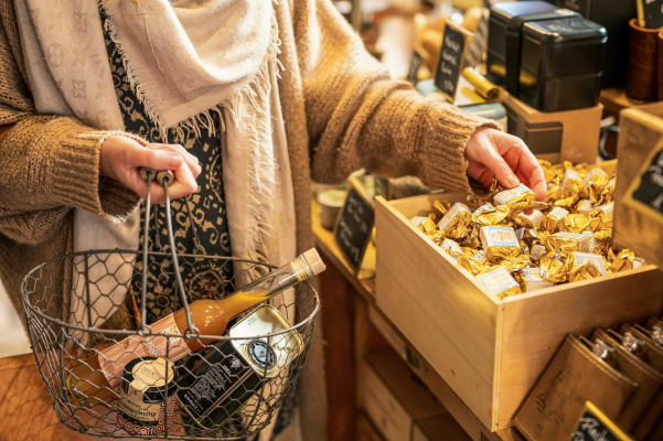 Hier wird eine Einkaufsszene gezeigt, in der eine Frau Süßigkeiten in ihren Einkaufskorb legt. Thema des Tourismusfotoshootings war die Genusstour durch Rostock in Mecklenburg-Vorpommern.
