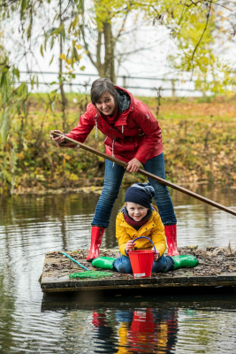 Foto für Tourismus-Marketing-Kampagne. Eine Frau steht mit einem Panel auf einem Floß. Unter ihr sitzt ein Kind. Man sieht, dass beide Spaß beim Paddeln auf dem See haben. Aussagekräftige Fotos für Ihre touristische Destination.