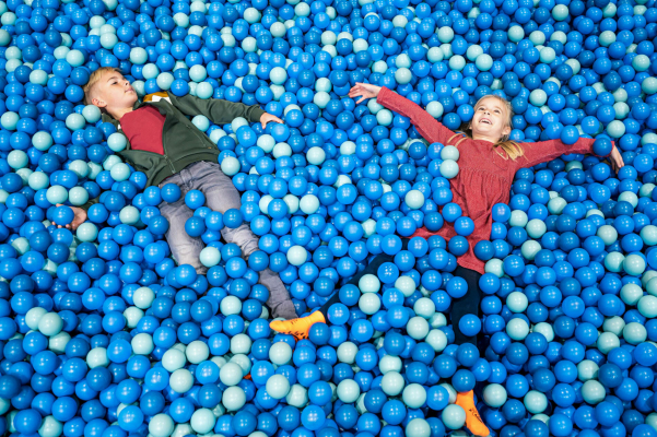 aussagekräftige Fotos für Ihr Unternehmen. Zwei Kinder liegen zwischen blauen Bällen im Kindertobeland.