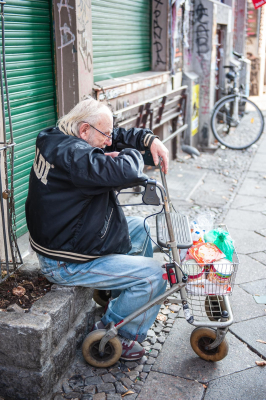 Ein alter Mann sitzt mit seinem Rollator und seinen Einkäufen in einer Berliner Straße