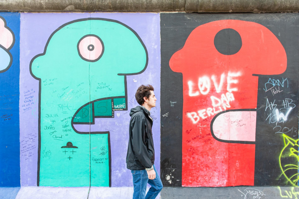 Ein junger Mann läuft die Berliner Mauer, die mit Graffitikunst bemalt ist, entlang.