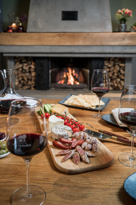 gedeckter Tisch am Kamin mit Wurst- und Käseplatte und Rotwein
