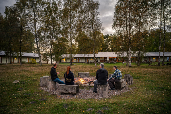 Gäste sitzen auf einer Wiese vor einem Hotel an einem gemütlichen Lagerfeuer
