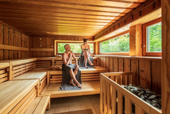 Hotelsauna BEECH Resort - Plauer See 2 Saunagäste in der hoteleigenen großen Sauna, die durch eine großes Fenster hinaus in die Natur sehen.
