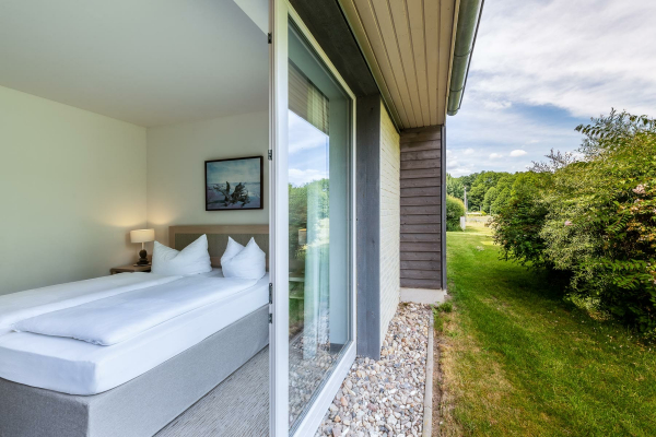 Hotelfoto von einem ebenerdigen Hotelzimmer mit weit geöffneter Balkontür, die den Blick in den Garten freigibt.