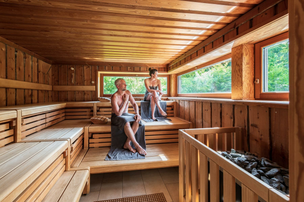 Foto von einem Hotel Fotoshooting. Aussagekräftige Fotos für Ihr Hotel-Unternehmen. Zwei Hotelgäste sitzen in einer Sauna und schauen durch die Panoramafenster hinaus in die Natur.