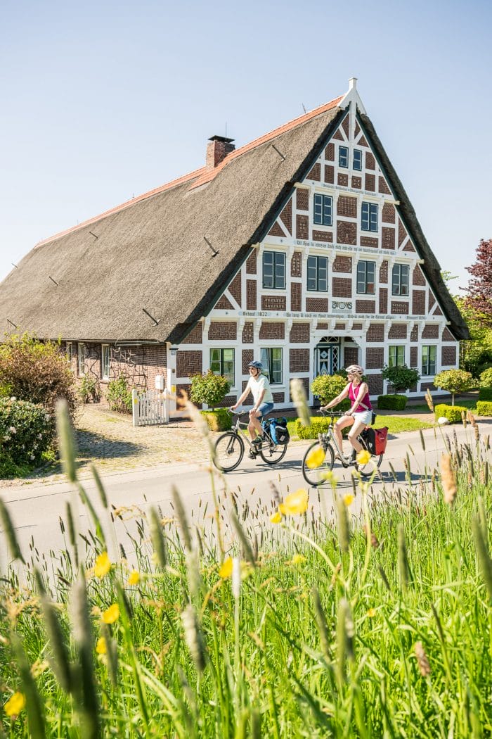 Fahrradfahrer Guderhandviertel zwei Fahrradfahrer fahren an einem herrlichen Tag im Sommer an einem schönen Fachwerkhaus in Landkreis Stade vorbei. Tourismusfoto aus der Kampagne des Mönchsweges um neue Fotos für die Wegseite zu erhalten.