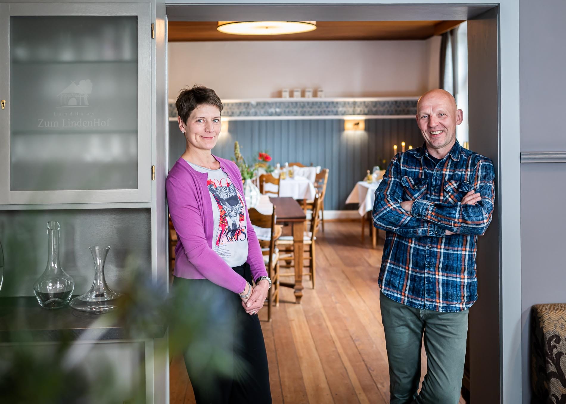 die Gastgeber Beccy und Tom vom LandHaus "Zum Lindenhof" stehen bei sich im Restaurant uns lächeln in die Kamera
