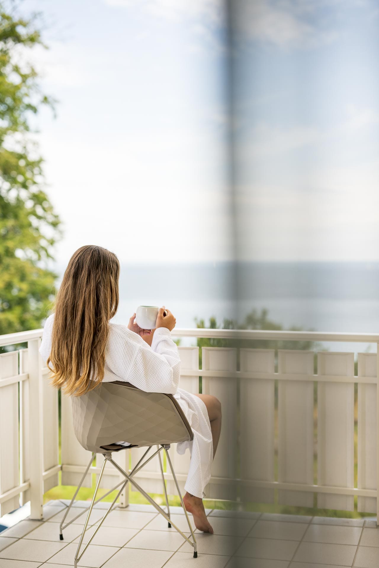 eine Frau sitzt auf einem Balkon eines Hotelzimmers und blickt aufs Meer hinaus