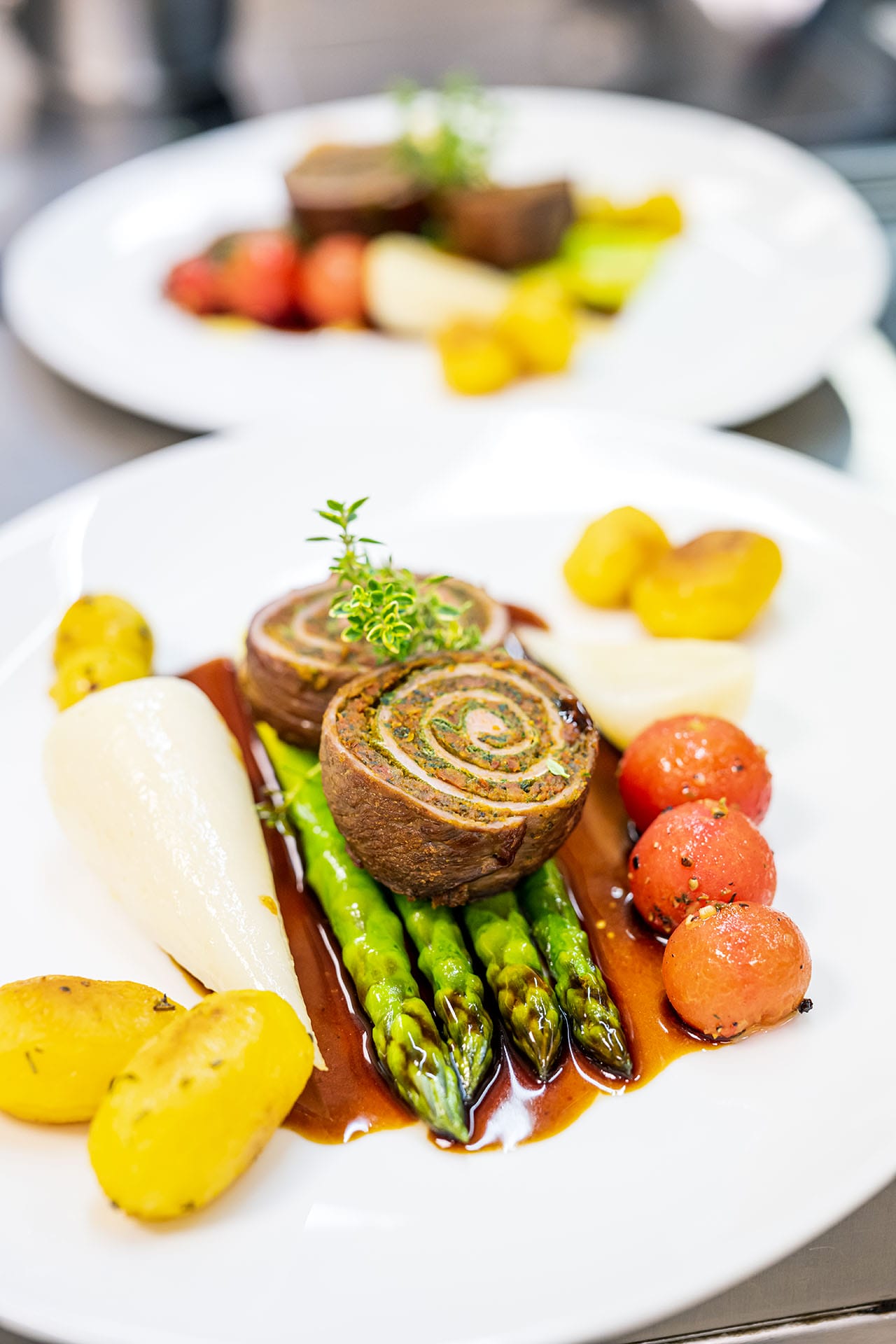 Ein Menü-Teller mit Spargel, Heidekartoffeln, Tomaten und oben drauf zwei Stücke geschnittene Heidschnucken-Rouladen