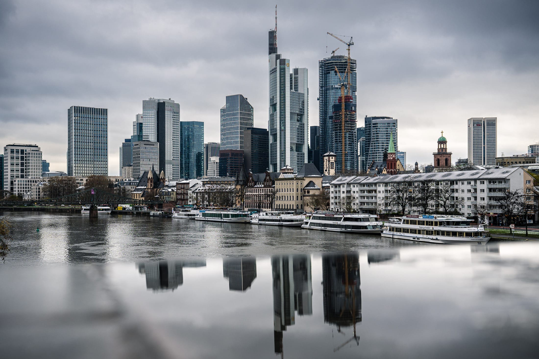 Frankfurter Skyline über den Main fotografiert. Im Vordergrund spiegelt sich die Skyline in einer Spiegelfläche
