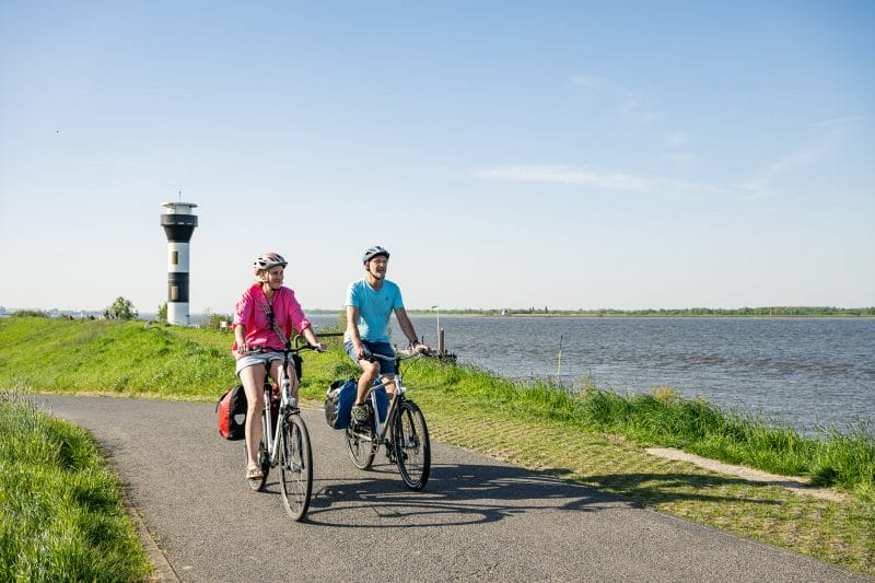 Twielenflether Leuchtturm Stade Fahrradfahrer fahren auf einem Elbe-Deich bei schönstem Wetter bei Stade entlang.
